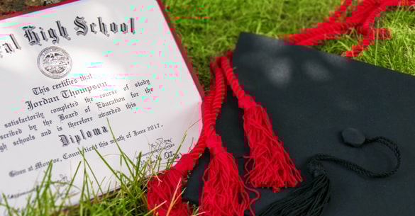 High School diploma sitting next to a graduation cap and red honor cord.