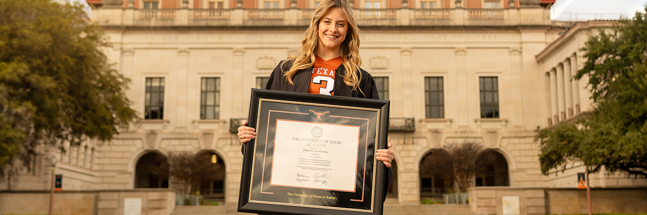 happy, smiling, blonde haired girl in graduation regalia and a Texas football jersey holding a Texas diploma frame.