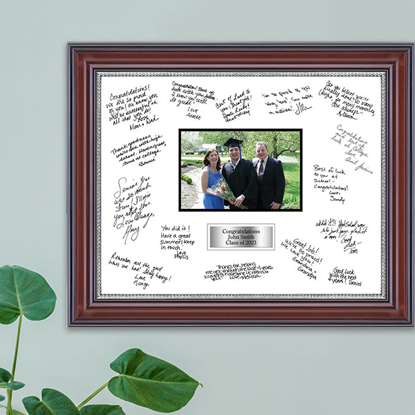 Autograph picture frame with photo of graduate and parents hanging on wall above plant
