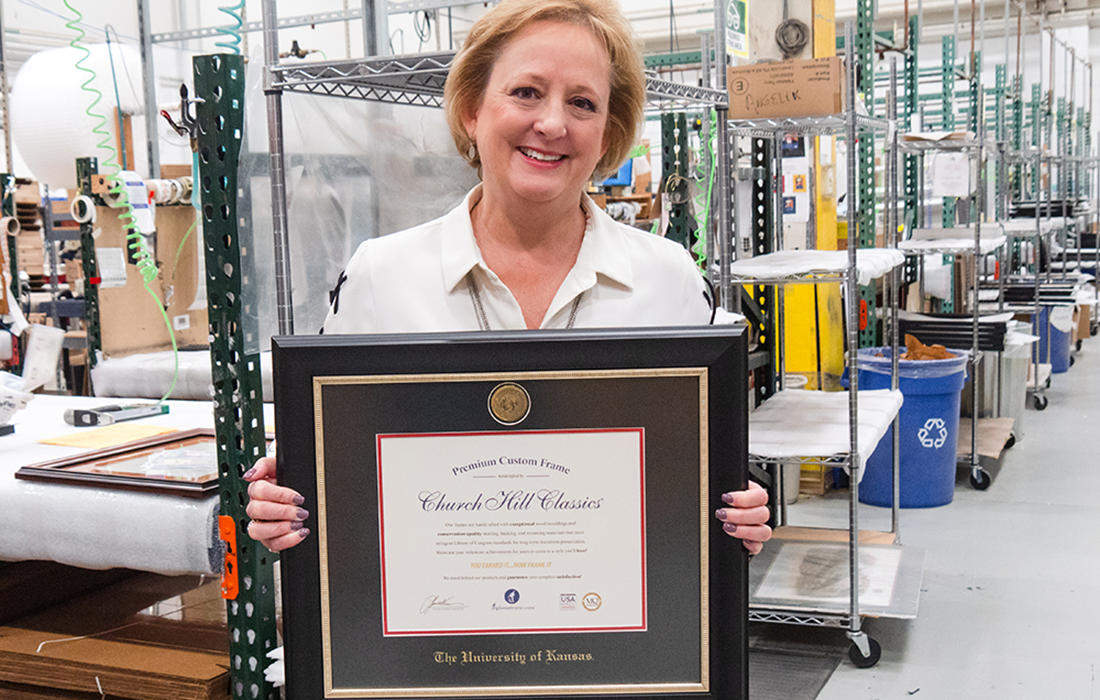 CEO Lucie Voves smiling while holding a custom certificate frame on the production floor