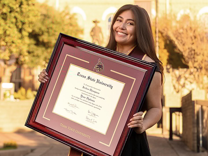 brown haired girl holding a church hill classics diploma frame for Texas State University