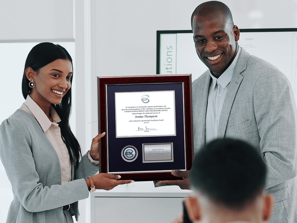 Two individuals presenting a custom frame with a medallion and engraved plaque during an employee recognition event