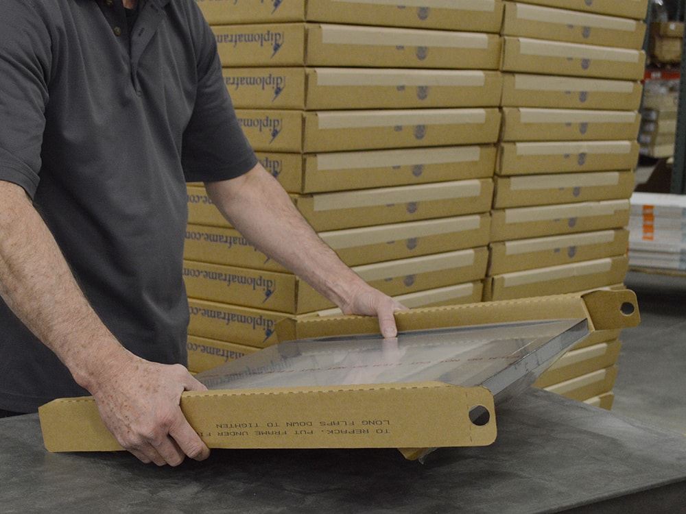 a person holding a certificate frame that is being boxed up to ship.