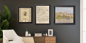 three framed art pieces in black frames above chair, plant, and dresser
