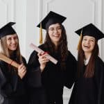 three female grads with rolled diplomas