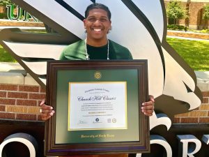 smiling student holding UNT degree frame on campus