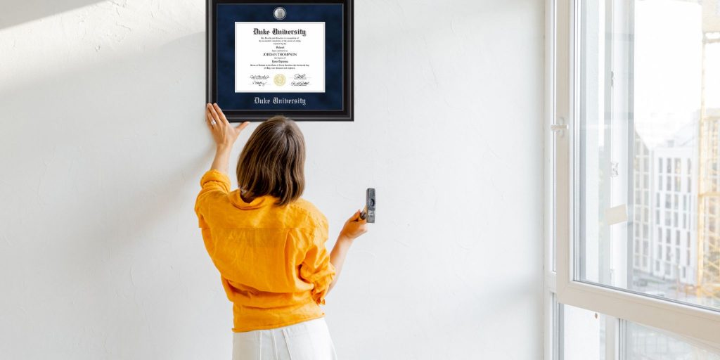 back of woman in yellow shirt hanging duke university diploma frame on wall