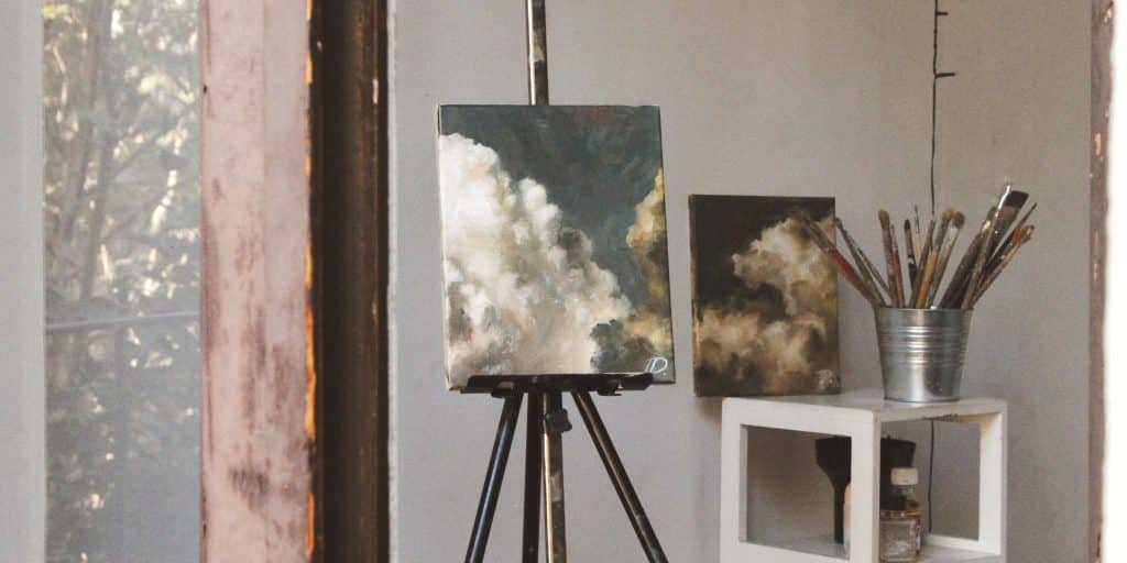 sky artwork on easel with other paintings in background