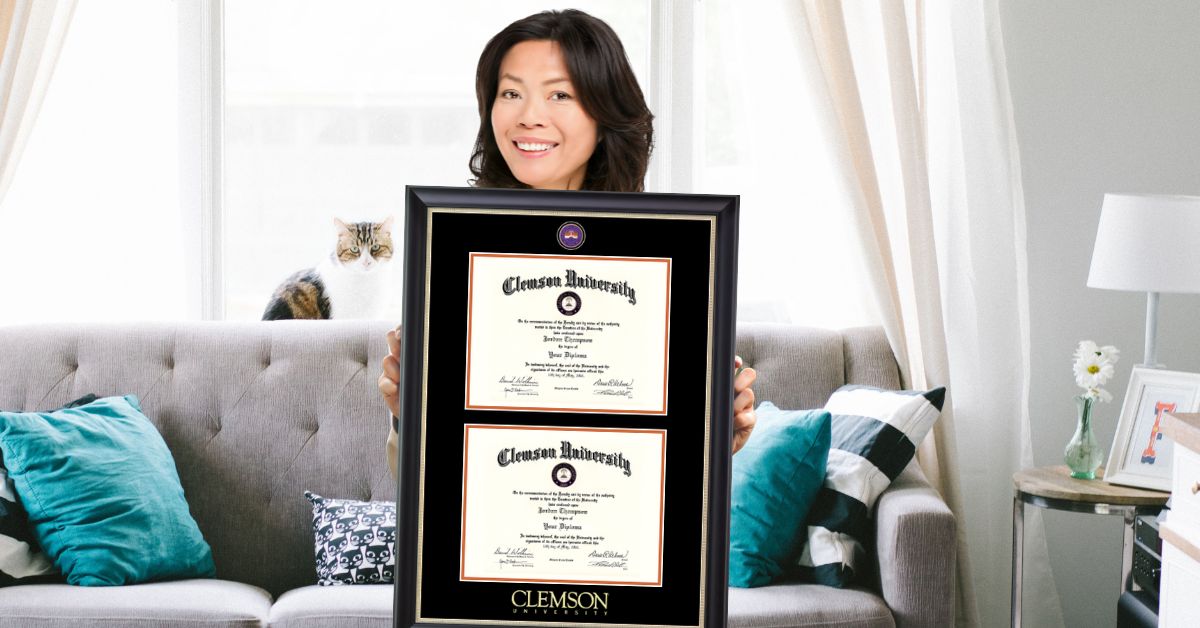 woman in living room holding Clemson double diploma frame