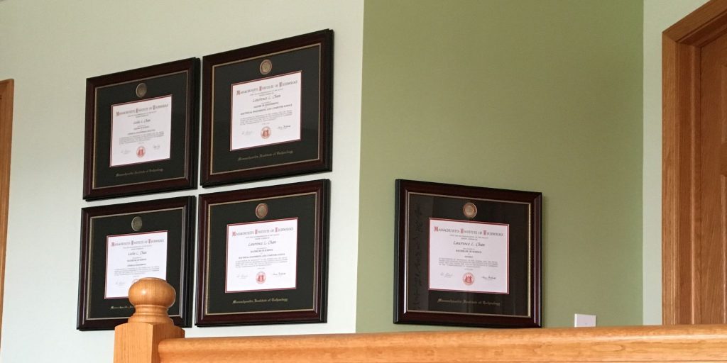 Five MIT degree frames hanging on green wall behind stair bannister