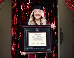 smiling graduate holding IUP diploma frame
