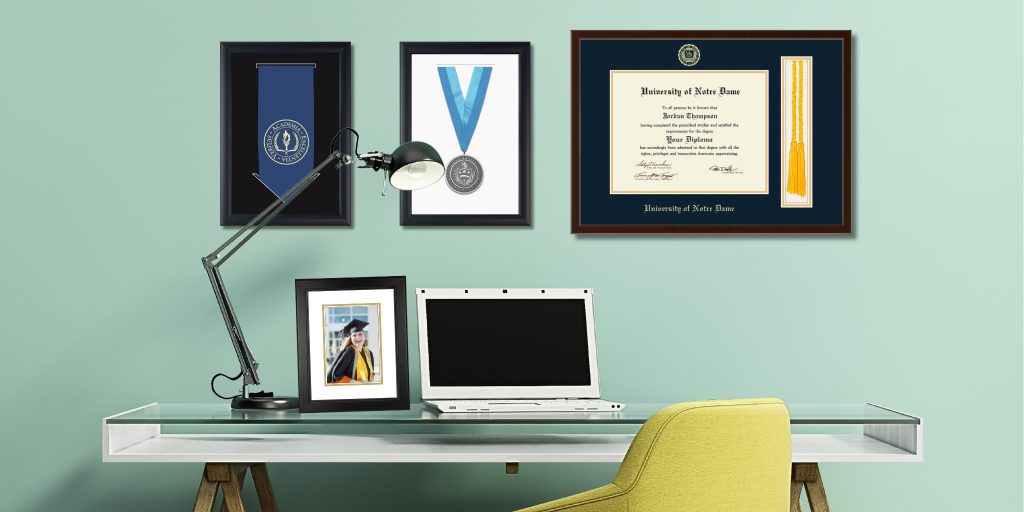 tassel diploma frame and regalia frames hanging on wall above desk with laptop and custom photo frame on it