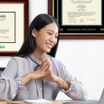 woman on laptop with marshall university diploma frames on wall