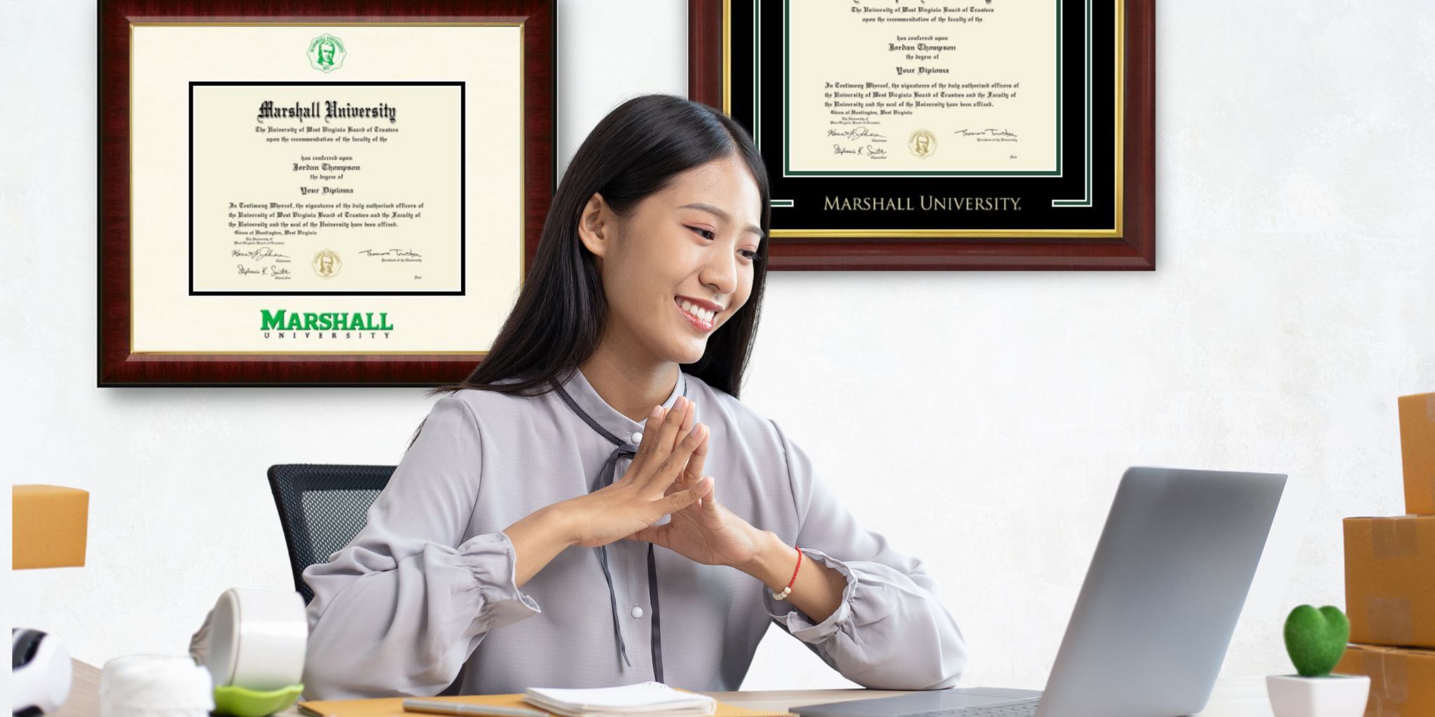 woman on laptop with marshall university diploma frames on wall
