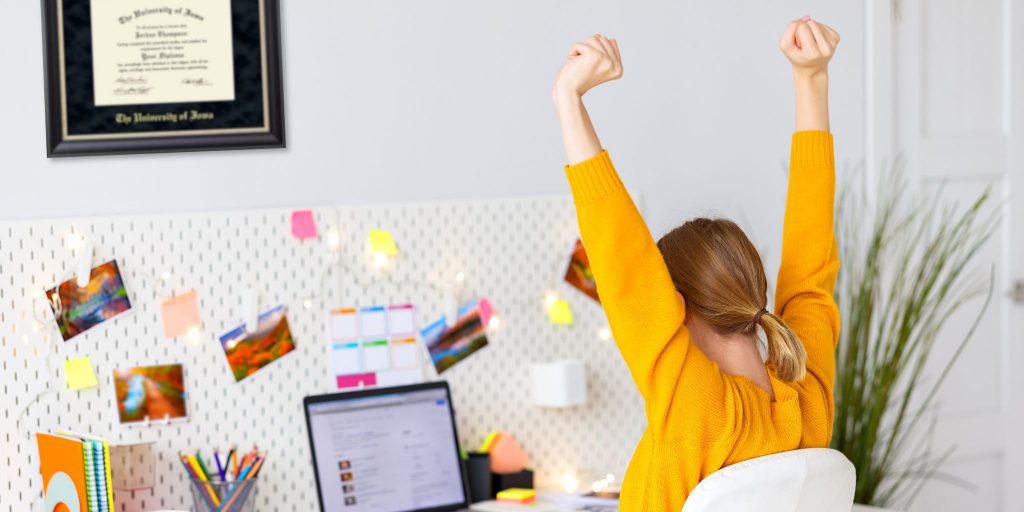 entrepreneur at desk cheering on success with diploma frame in background