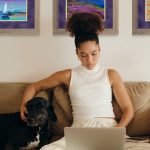 girl on couch with dog working on laptop
