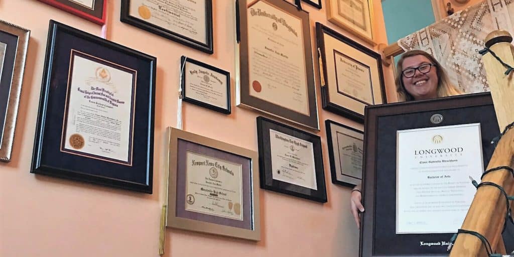 woman on staircase with wall covered with diploma frames