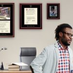 man in front of desk with harvard diploma frames on wall