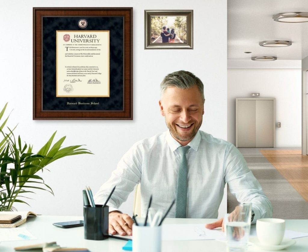 man working at desk with Harvard business school frame on wall