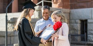 mother and father gifting a custom diploma frame to their daughter in college graduation regalia