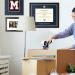 college senior packing boxes with frames on wall