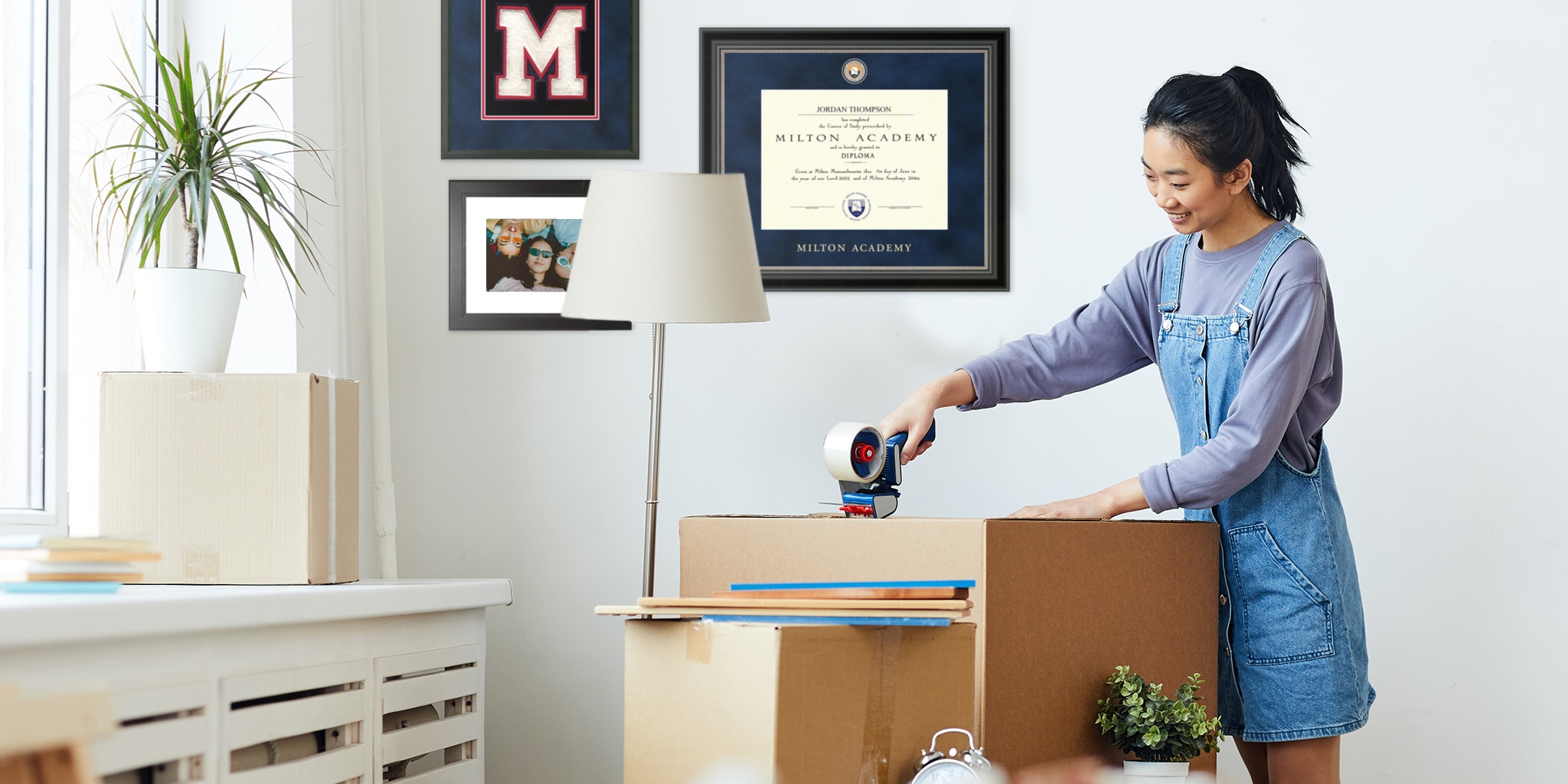 college senior packing boxes with frames on wall