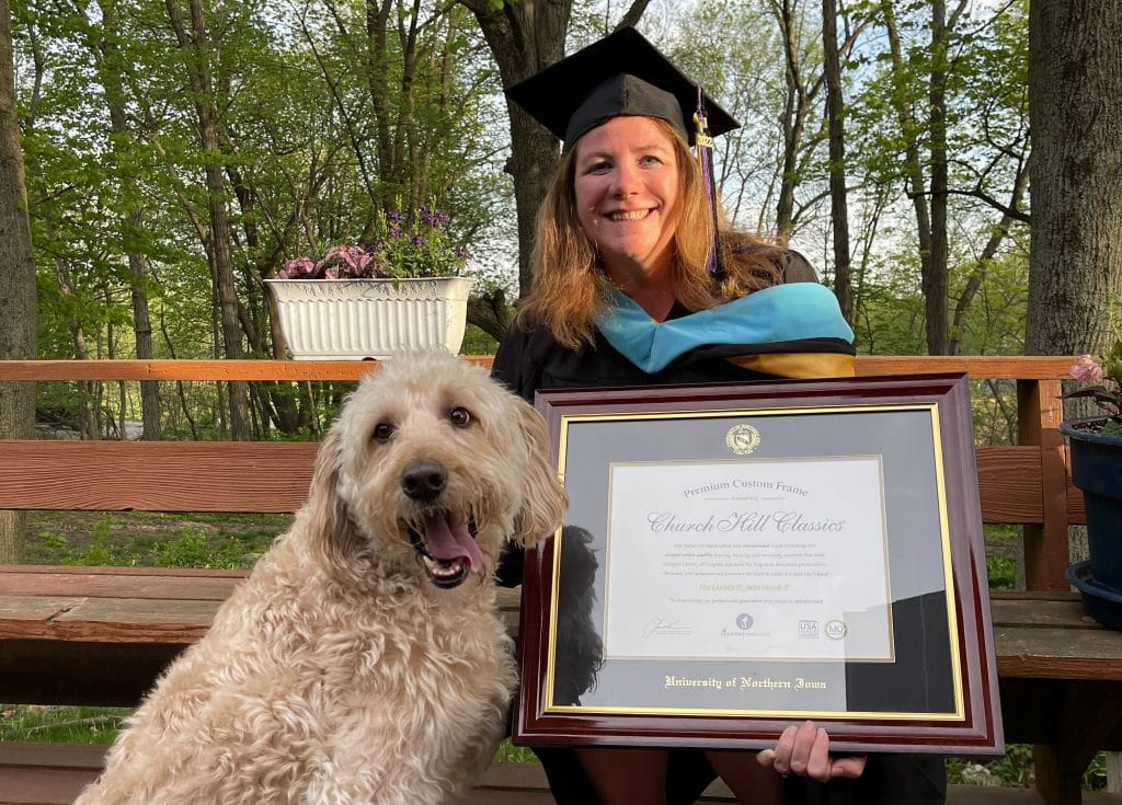 UNI graduate smiling with custom frame and dog