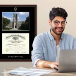 man working at laptop with custom diploma frame and medal shadow box on wall behind him
