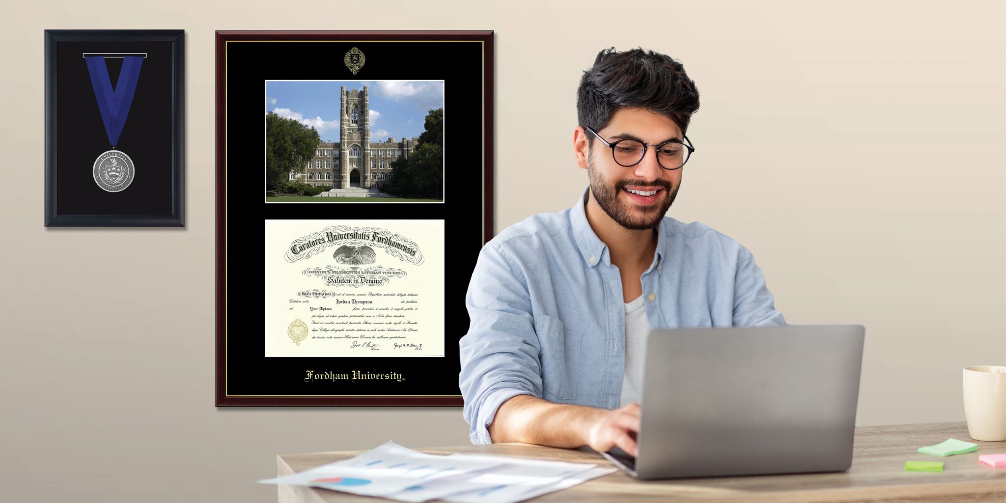 man working at laptop with custom diploma frame and medal shadow box on wall behind him