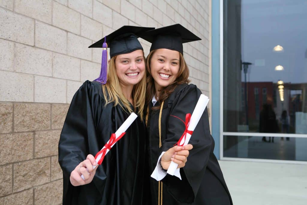 two female grads holding diplomas
