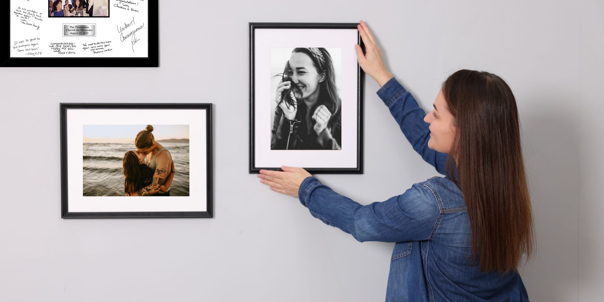 Woman hanging black photo frames of herself and fiance on gray wall