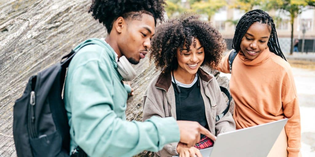 three students outside looking at laptop