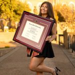 smiling Texas State University graduate holding a custom TSU diploma frame
