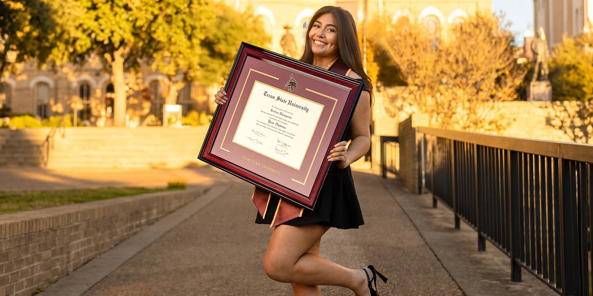 smiling Texas State University graduate holding a custom TSU diploma frame