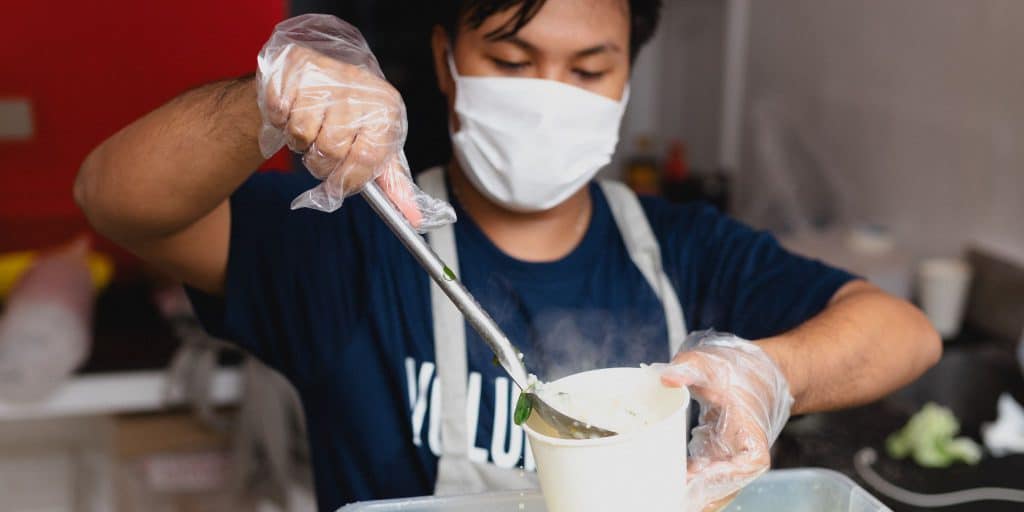 student in mask volunteering at soup kitchen