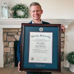 smiling man holding Liberty University diploma frame