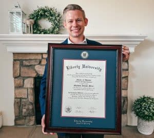smiling man holding Liberty University diploma frame