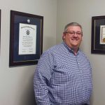 man standing next to his charleston southern and USC diploma frames and CPA certificate frame on gray wall