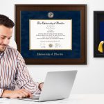 businessman working on computer with presidential diploma frame and doctoral tam shadow box hung on wall behind him in office