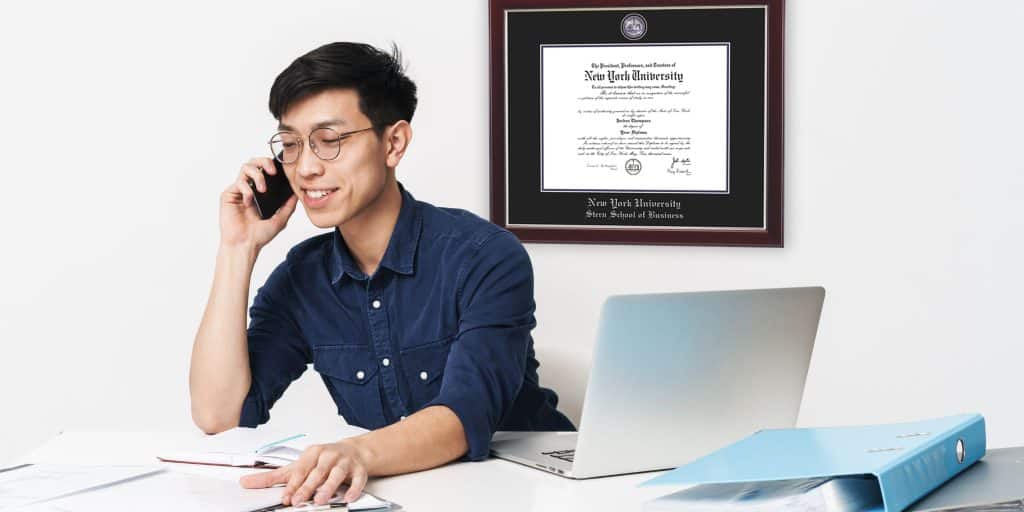 businessman on phone call with NYU business diploma frame behind on wall