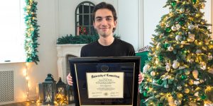 young man holding uconn diploma frame in front of christmas tree