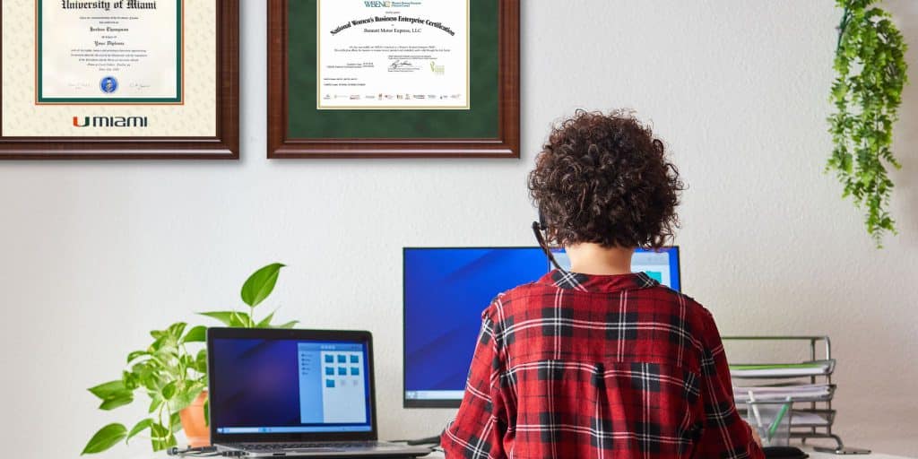 woman on laptop with framed credentials on wall