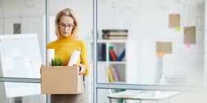 woman in yellow holding box walking out of office