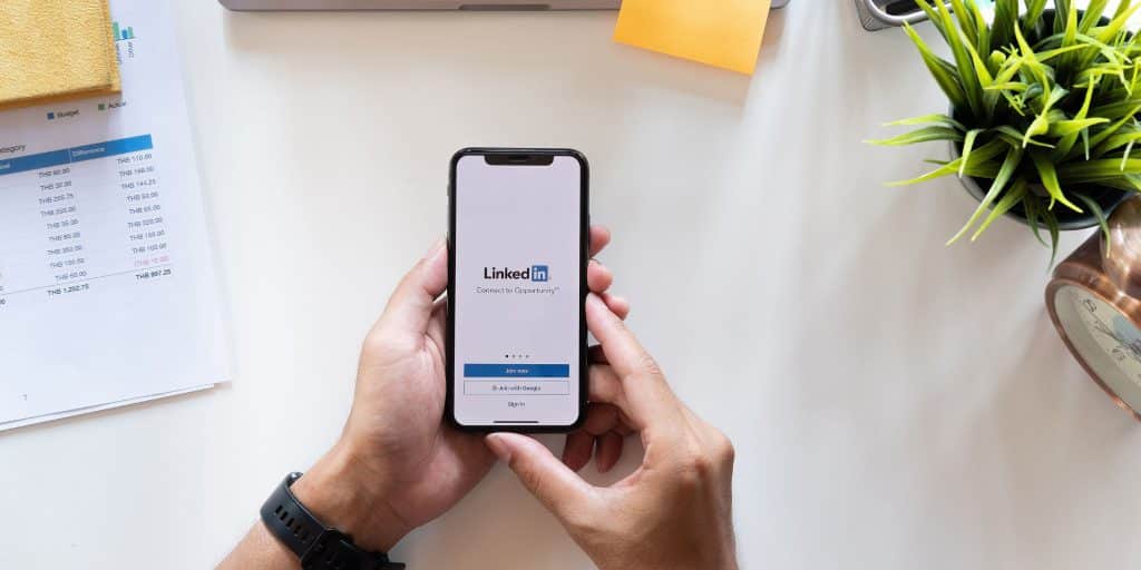 image of hand holding phone with linkedin pulled up over desk