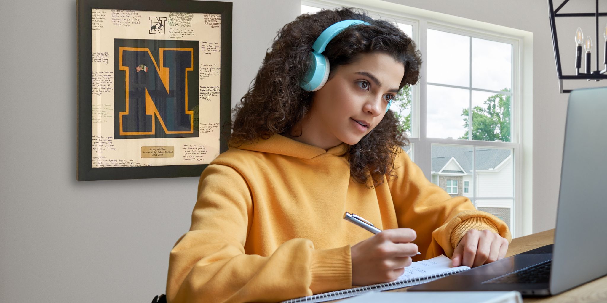 girl with headphones working on laptop with varsity letter frame on wall