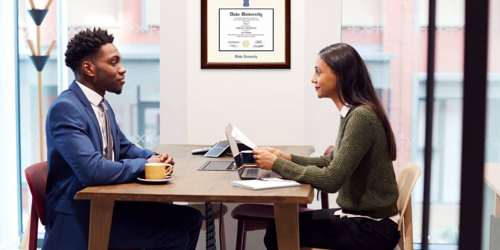 Hiring manager interviewing candidate with Duke University diploma frame on office wall