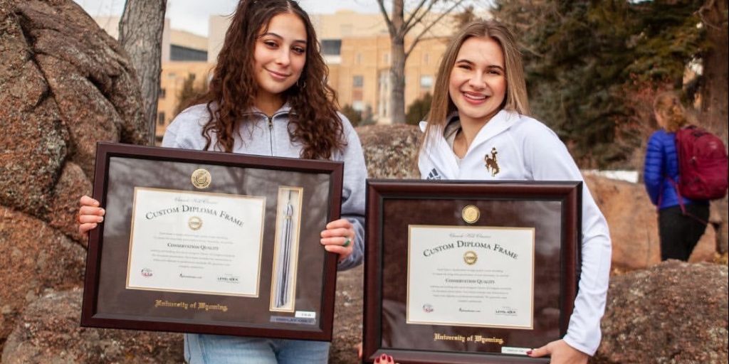 two university of wyoming female graduates standing outside with custom diploma frames