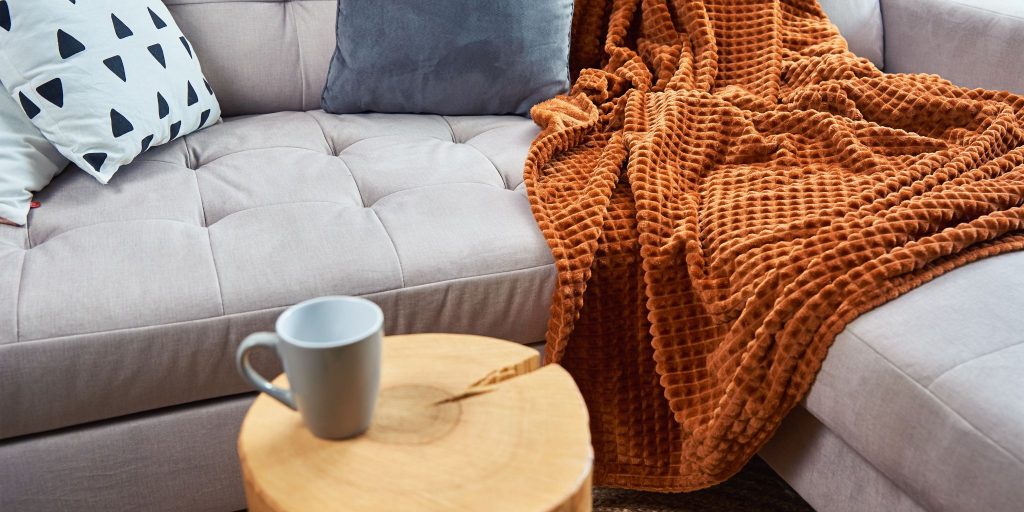 orange blanket on a couch next to coffee table with coffee on it