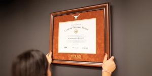 back of woman's head who is hanging UT Austin diploma frame on wall