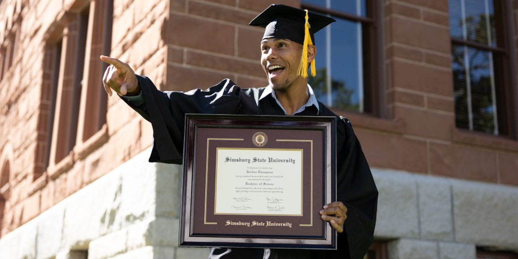 happy graduate holding diploma frame pointing at something ahead of him